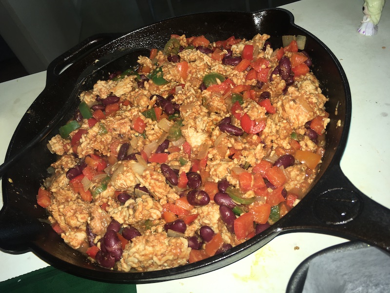 a cast iron frying pan containing cooked chicken mince, capsicum, chillies and beans