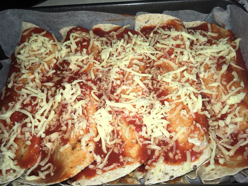 a roasting pan with five enchiladas in it, covered in tomato puree and shredded cheese