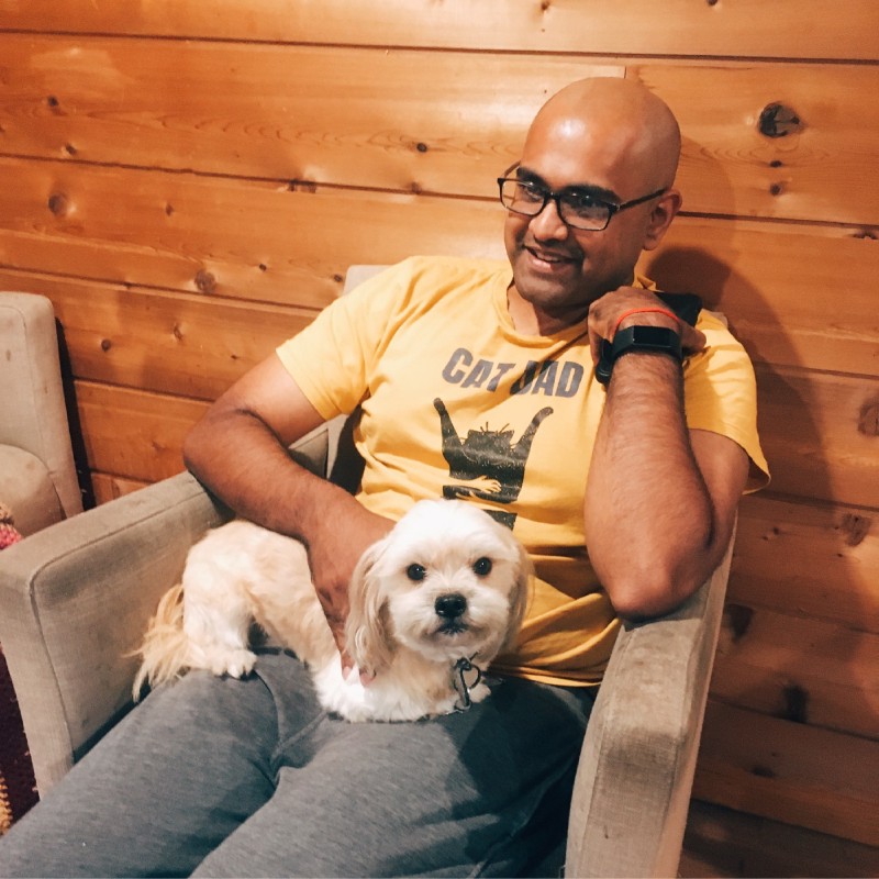 a small white dog looks at the camera from the lap of a young man in a yellow t-shirt