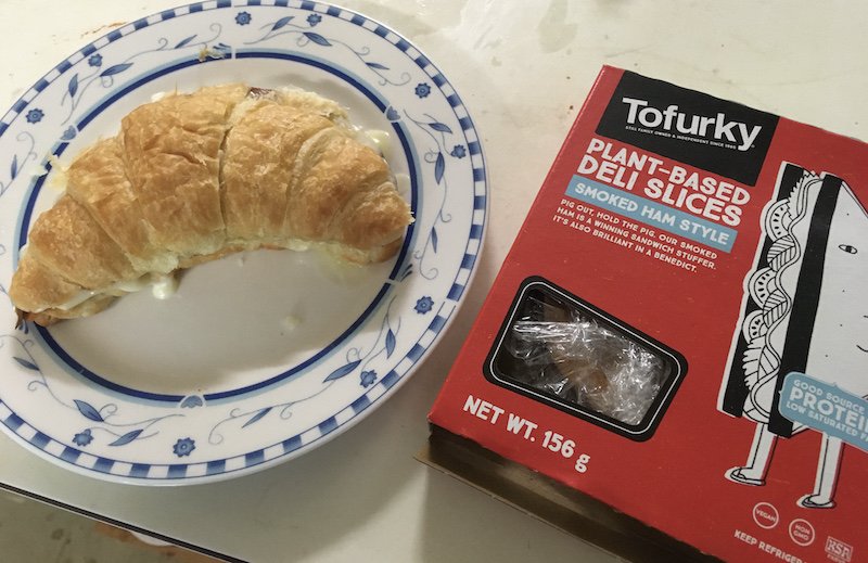 a small plate with a ham and cheese croissant, and a package of Tofurky smoked ham slices