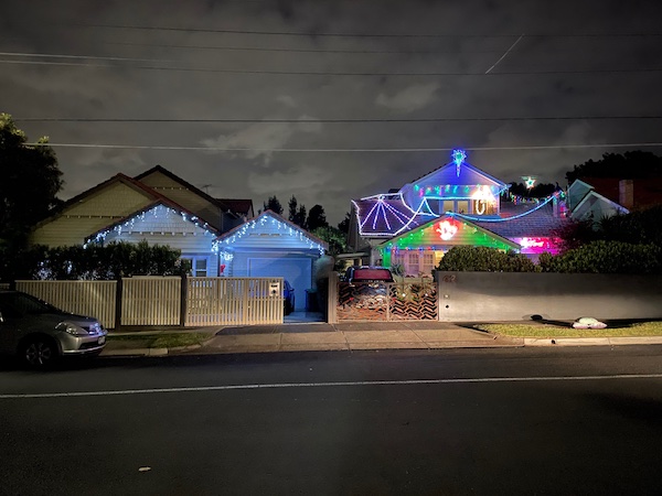 a 1920s house with white lights hanging from the eaves and colourful ones on the fence