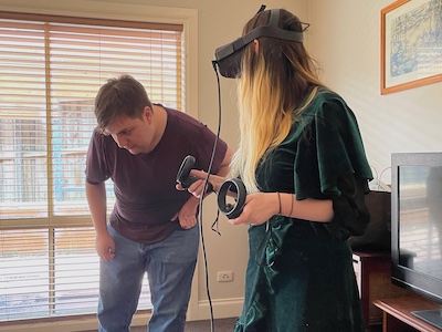 a young woman in a VR headset and a slightly older man bending over to check an (off-camera) screen
