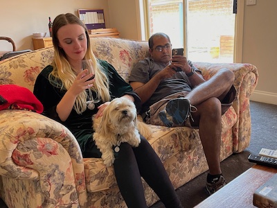 a young woman and young man on a couch, both on their phones; the woman has a dog on her lap
