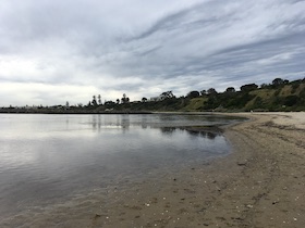 a view of calm ocean water, with some sand visible on the right-hand side and green hills behind
