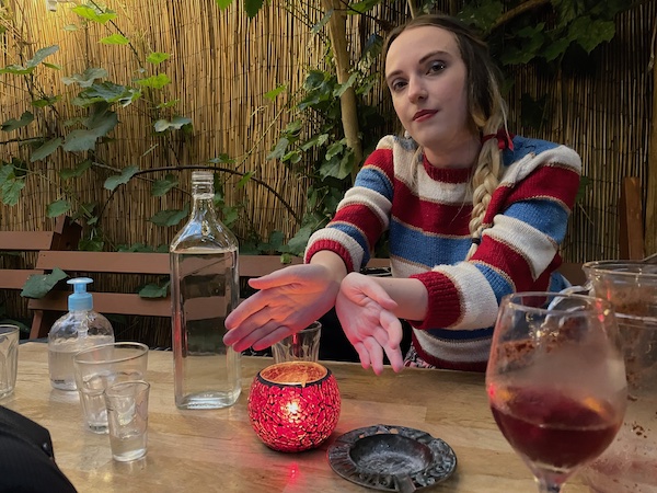 a photo of a young woman in make-up and a woollen jumper warming her hands over a candle on the table