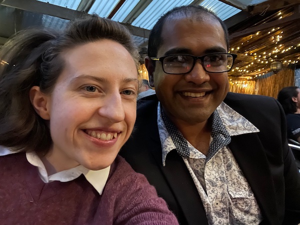 a photo of a young man and woman in a beer garden around sunset, both smiling broadly