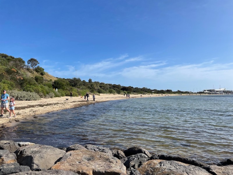 a shot of a beach, sand and grassy hill behind to the left, marina behind to the right
