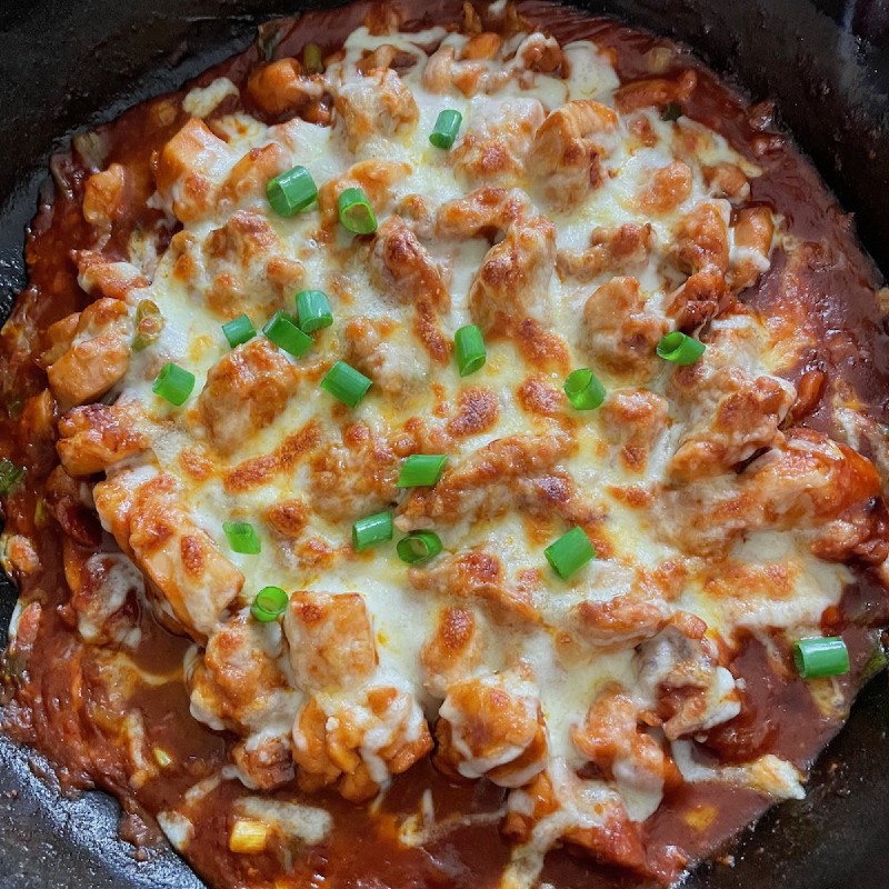 a cast-iron pan containing a chicken dish in red sauce, topped with melted mozzarella and sprinkled with spring onions
