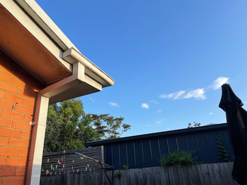 view of a blue sky with a single white cloud, with a red brick building to the left and a wooden fence (with washing line) at the bottom of the frame