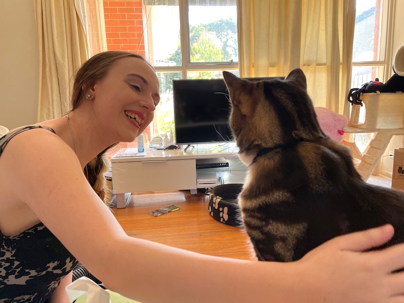 a young woman smiles as she pats a tabby cat