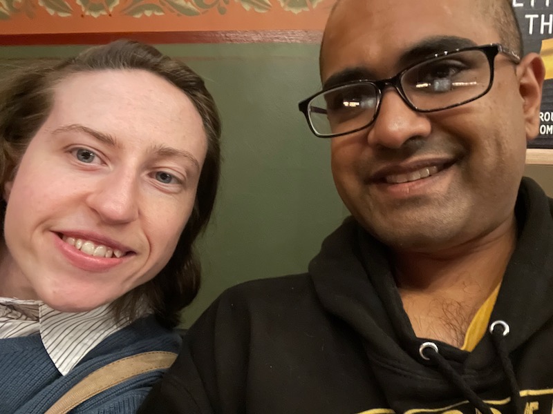 a selfie of a brunette white woman and bald bespectacled Indian man