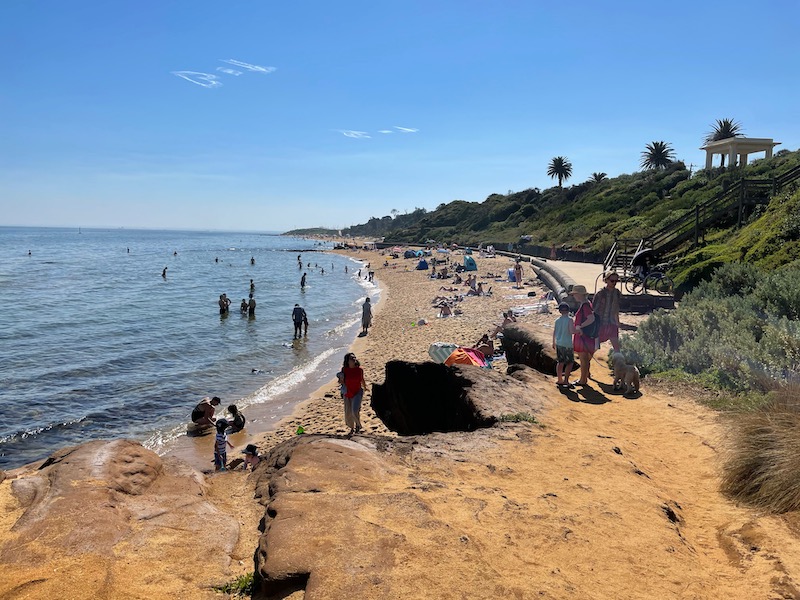 a wide shot of the ocean, beach and green hills, a pavilion in the distance