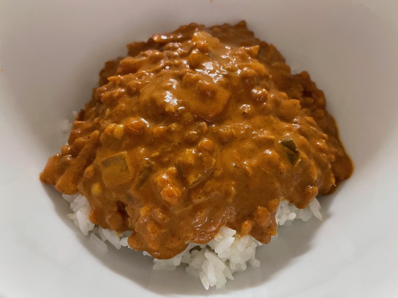 a bowl with a red-brown lentil stew atop some boiled white rice