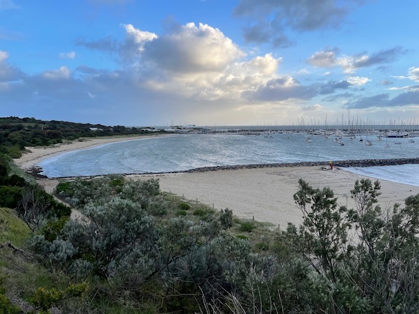 photo of a beach with partly cloudy skies above; coast on the left