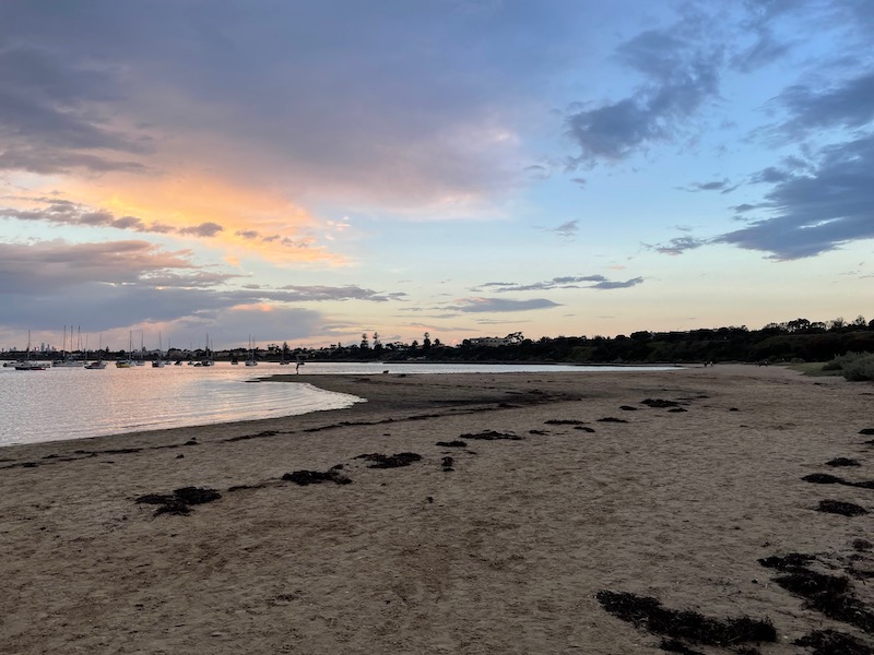 a view on the beach. a dark grey cloud to the left in the sky, with light blue and pink around it