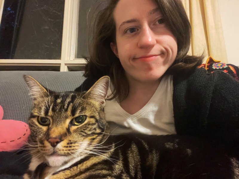 a young woman and a tabby cat sitting on a couch together, the cat on the woman's lap